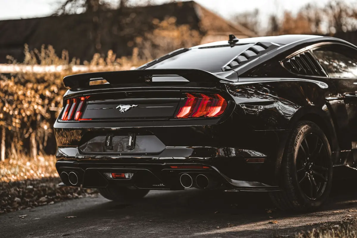 Crni Ford Mustang iz stražnjeg kuta na cesti prekrivenoj lišćem